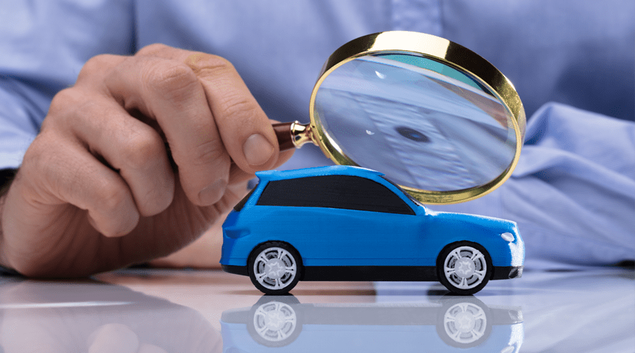 Close-up Of A Person's Hand Holding Magnifying Glass Over Small Blue Car